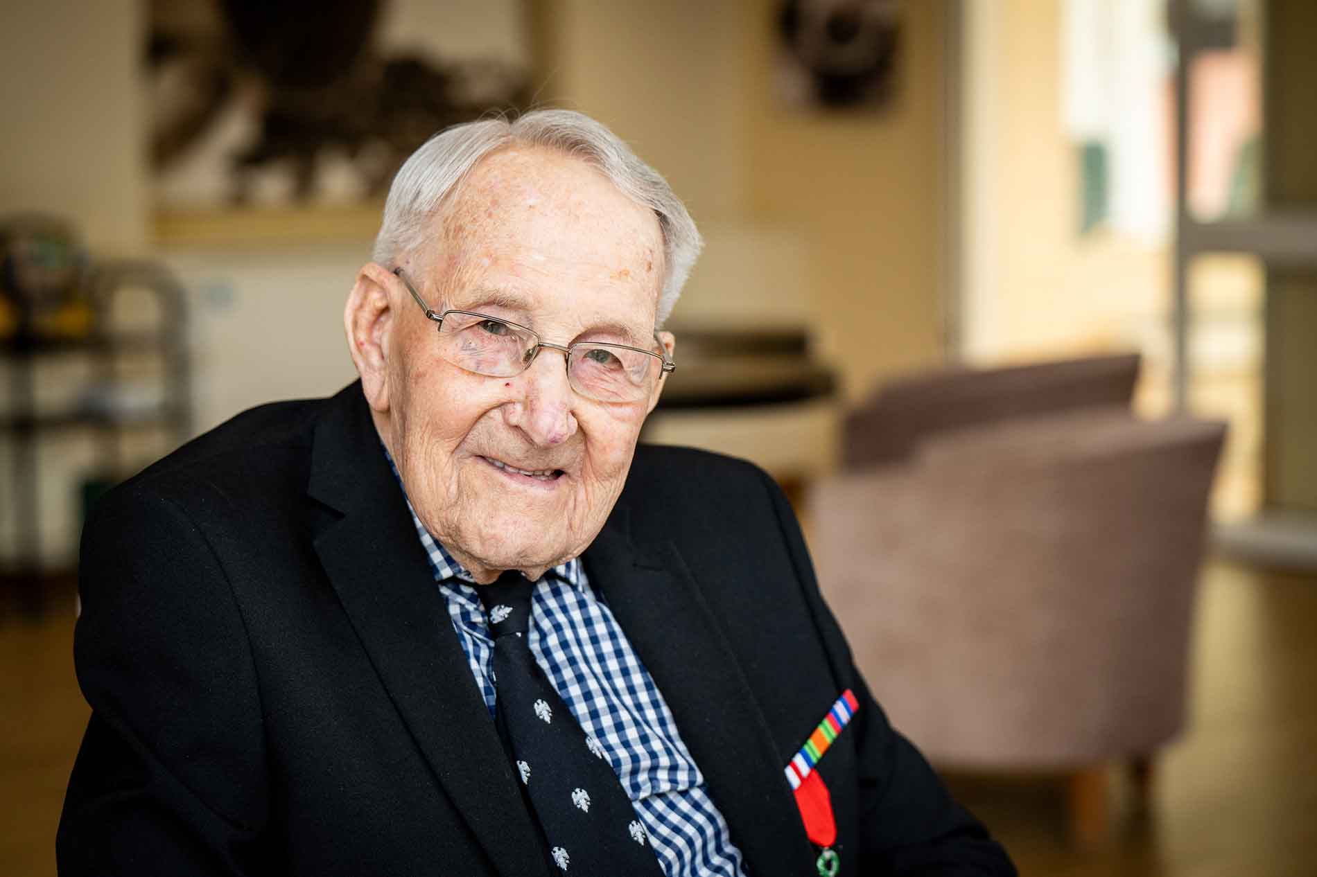 Male World War 2 veteran in glasses smiling at camera, wearing tie and medals