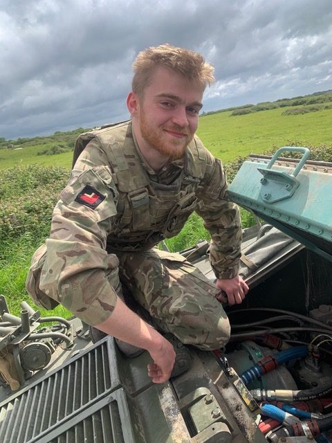 Young male soldier looking at engine of Warrior tank