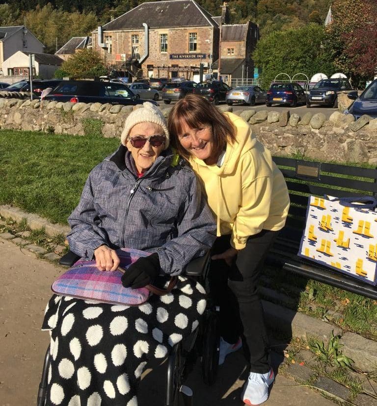 Elderly woman in wheelchair with smiling female volunteer outside