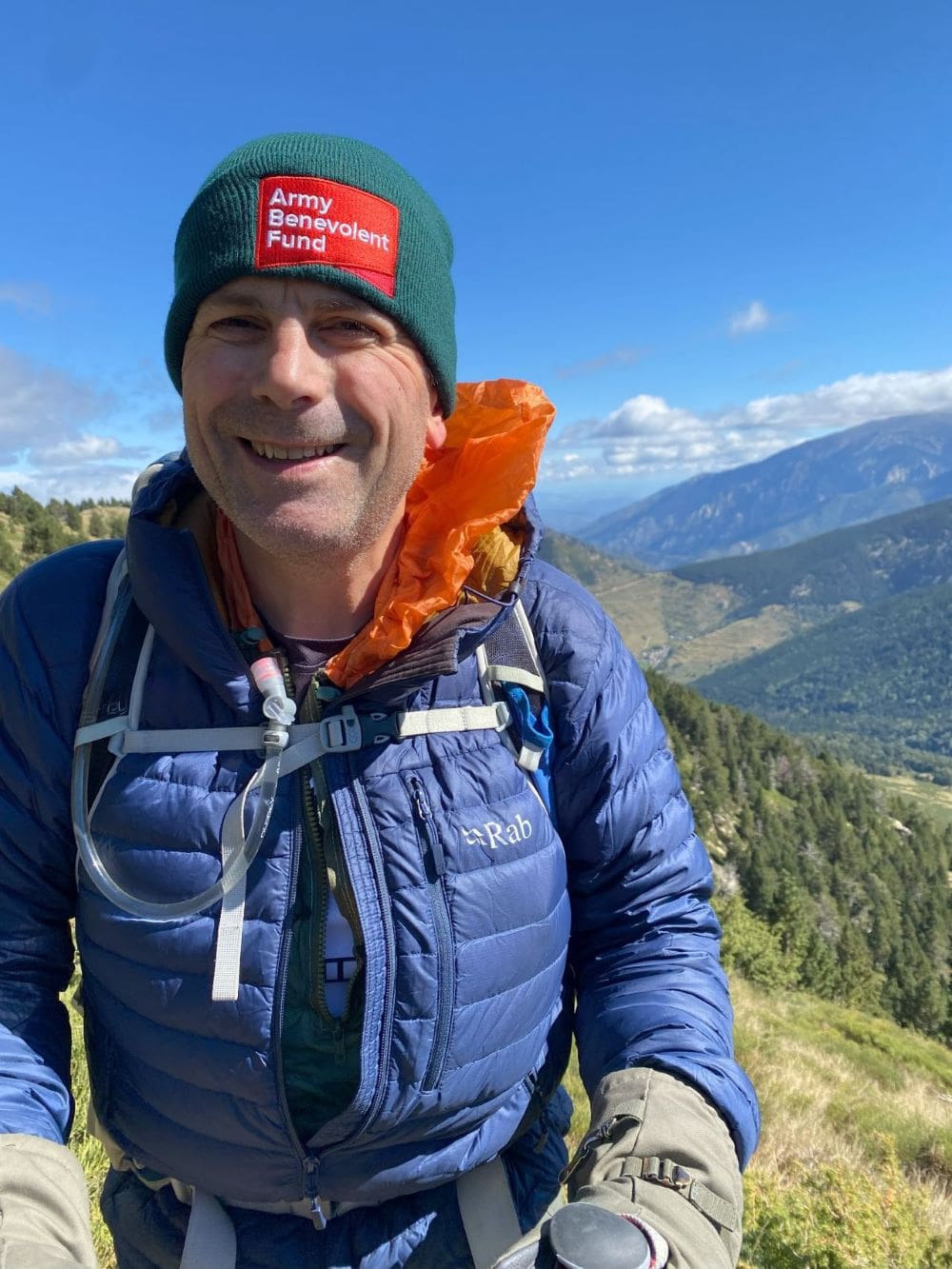 Man wearing beanie hat with Army Benevolent Fund logo at top of mountain